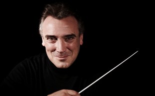 Man dressed in black on a black background holding a baton.