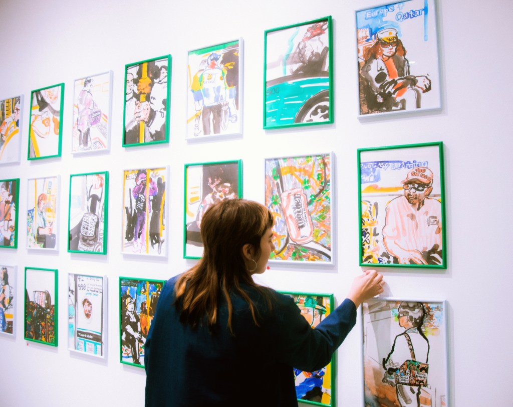 A yoougn female adjusting artworks on the wall of a gallery