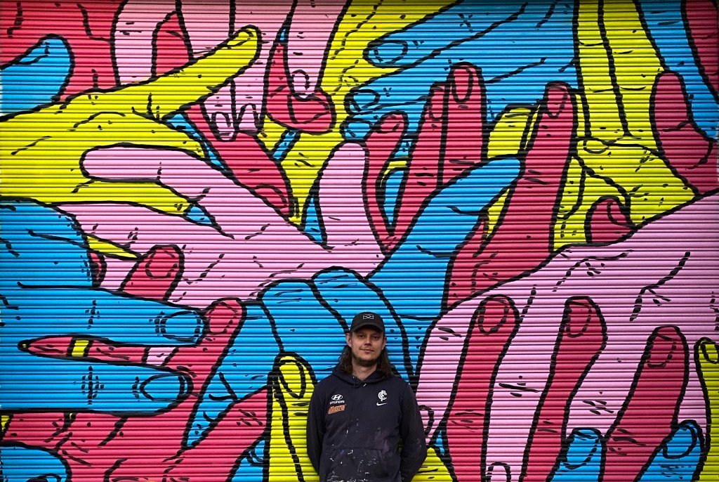 Indigenous person standing in front of a colourful mural