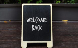 Back board with text reading Welcome Back with an autumn leaf under the board