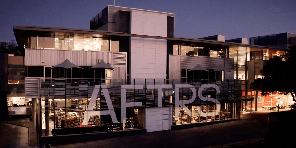 A lit building with a white neon sign reading AFTRS