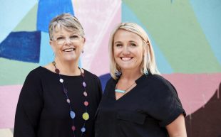 two women standing in front of a colourful wall