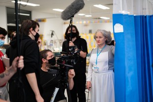 A film set in a hospital with a nurse and several camera operators surrounding her.