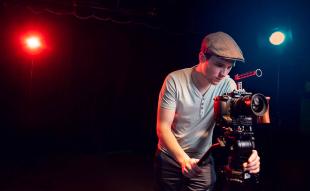 A camera man in a dark room with a red and blue light behind him