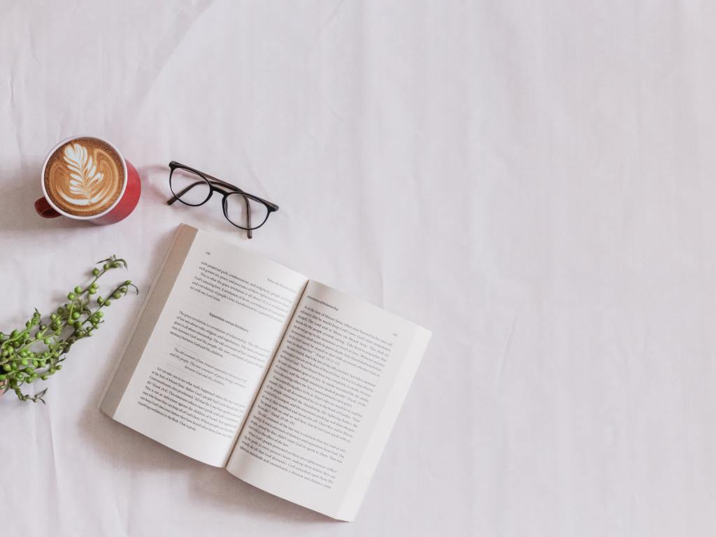 An open book on a table with a cup of coffee and reading glasses