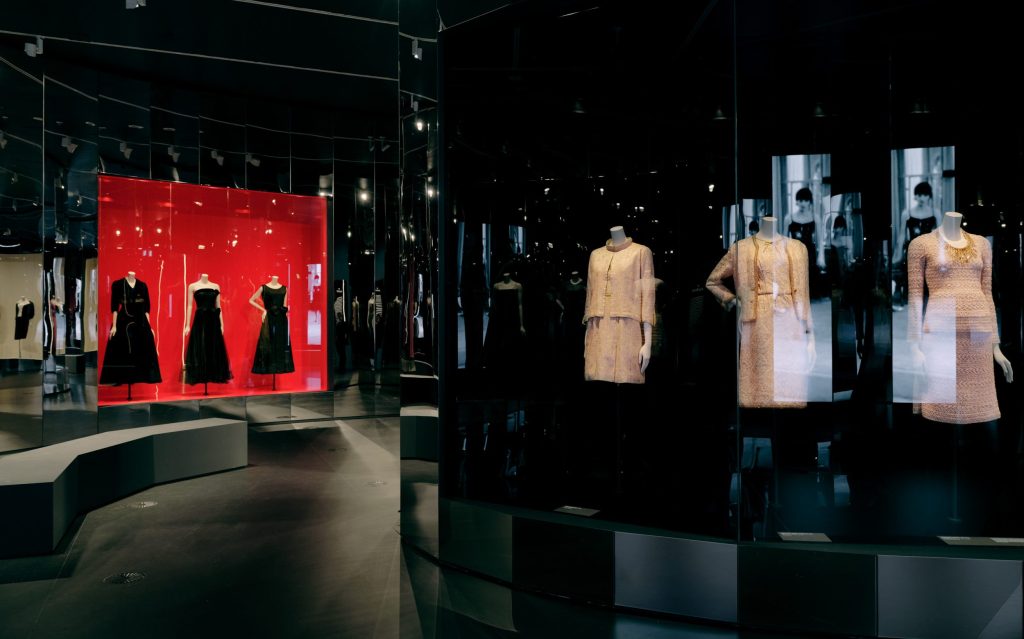 Dark exhibition space with three dresses displayed on the right.