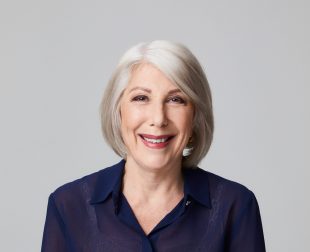 A grey-haired woman in a purple dress on a grey background