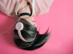 A young women with pink headphones on against a pink wall