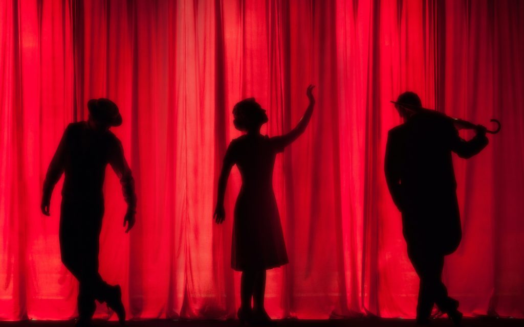 the silhouettes of three performers in front of a red curtain