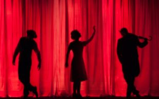 the silhouettes of three performers in front of a red curtain