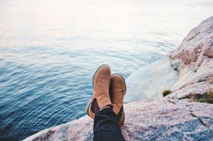 A man's legs outstretched over a cliff by the ocean