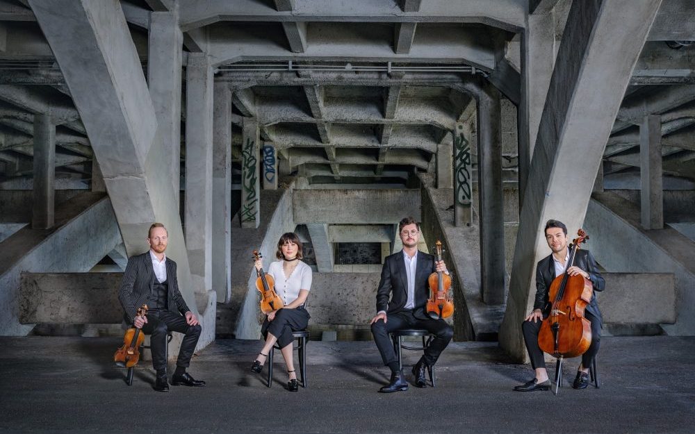 The four members of the Australian String Quartet sit under a bridge holding their instruments.