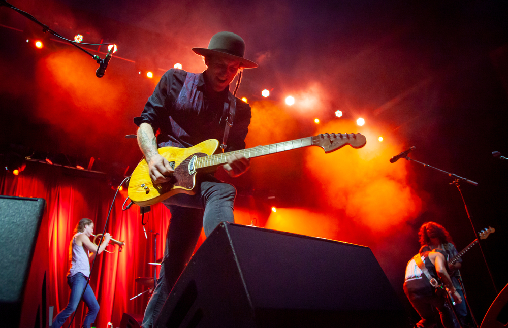 A guitar player stands with one foot on a foldback speaker as he plays.