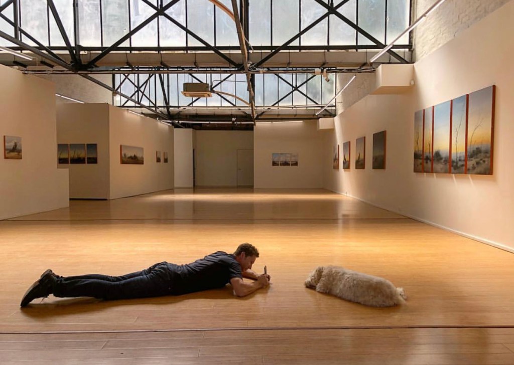 Man laying in art gallery with dog.
