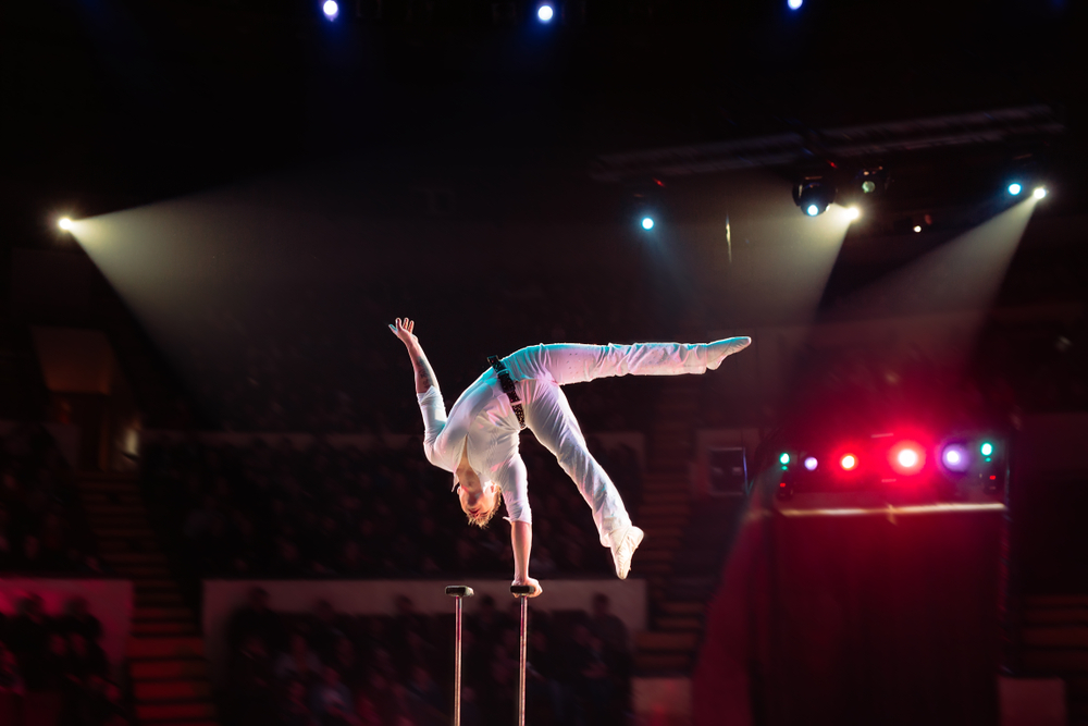 An acrobat balances on one hand with his legs in the air as part of a circus show.