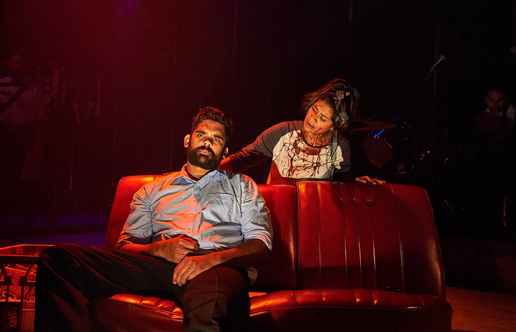 Two First Nations actors one sitting on a couch, the other covered in blood.