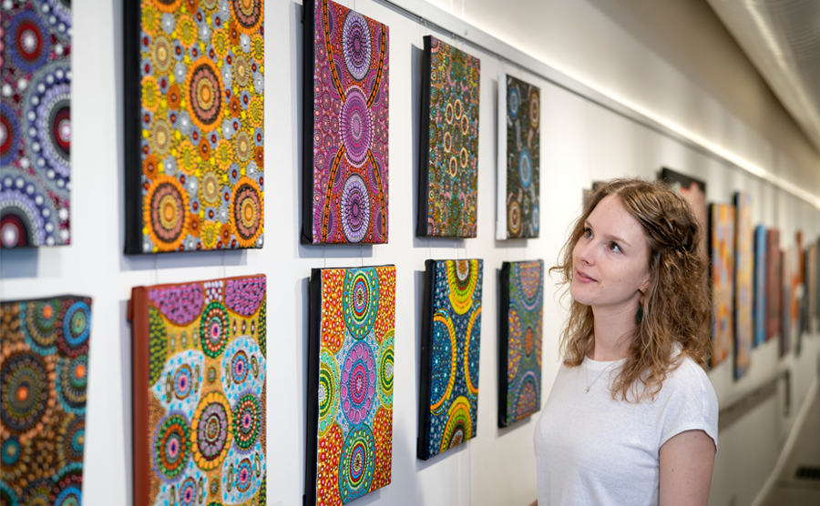 Woman looks at canvases on wall of First Nations artwork