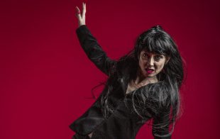 A woman in black in a pose of falling against a red backdrop