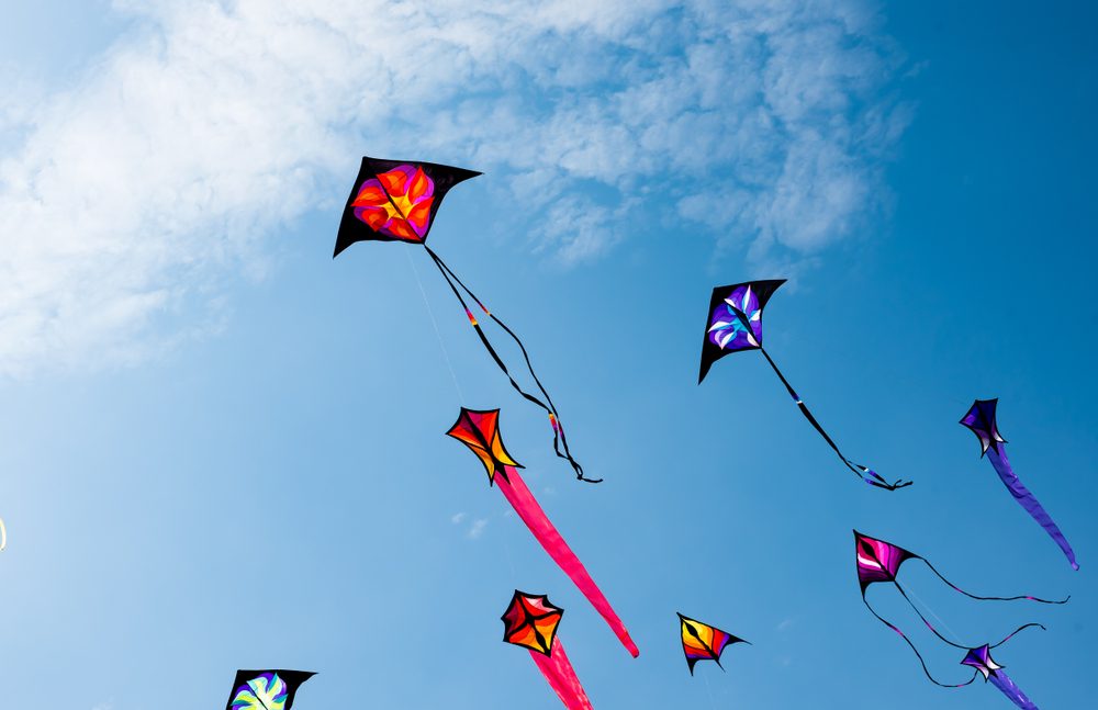 Brightly coloured kites fly against a blue sky dotted with clouds.