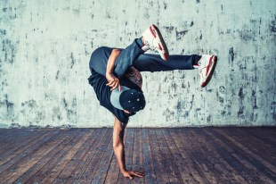 A male breakdancer balances on one hand.