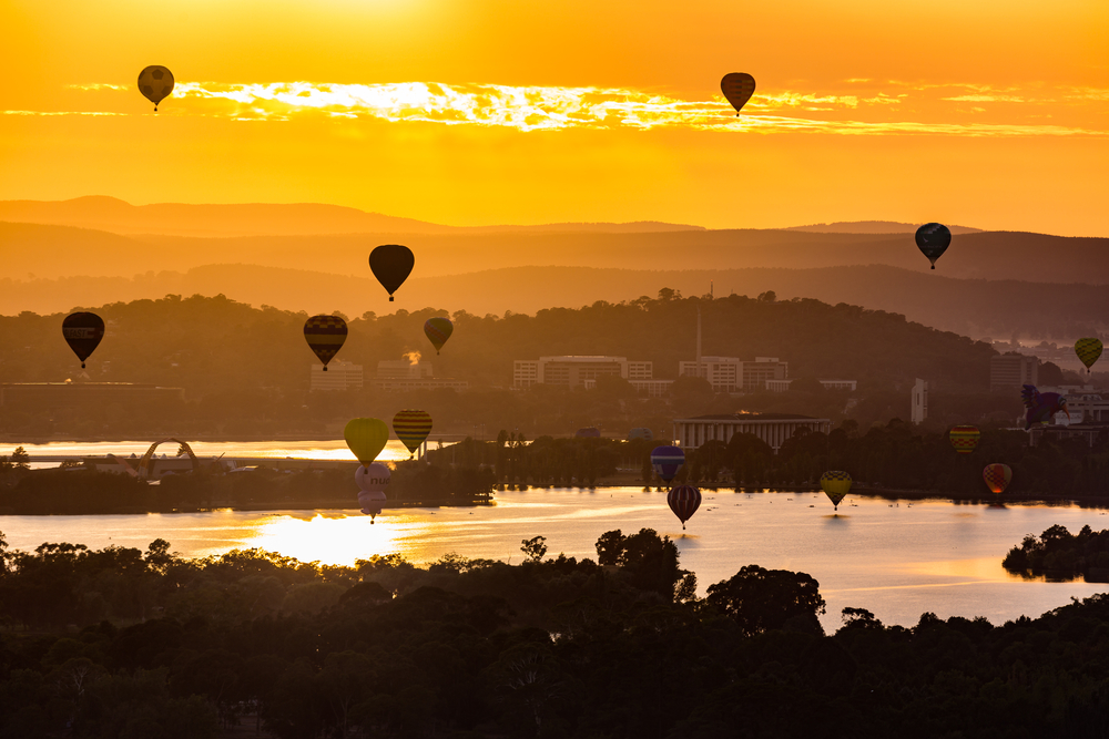 Hot air balloons float over Lake Burley Griffin in Canberra at dawn.