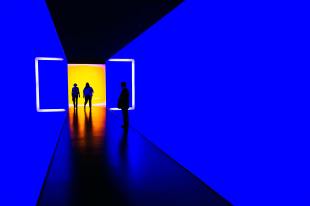 a bright neon lit gallery corridor space with two people in it.