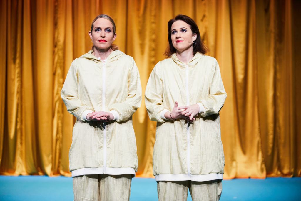 Two female performers onstage in front of a yellow stage cutrain