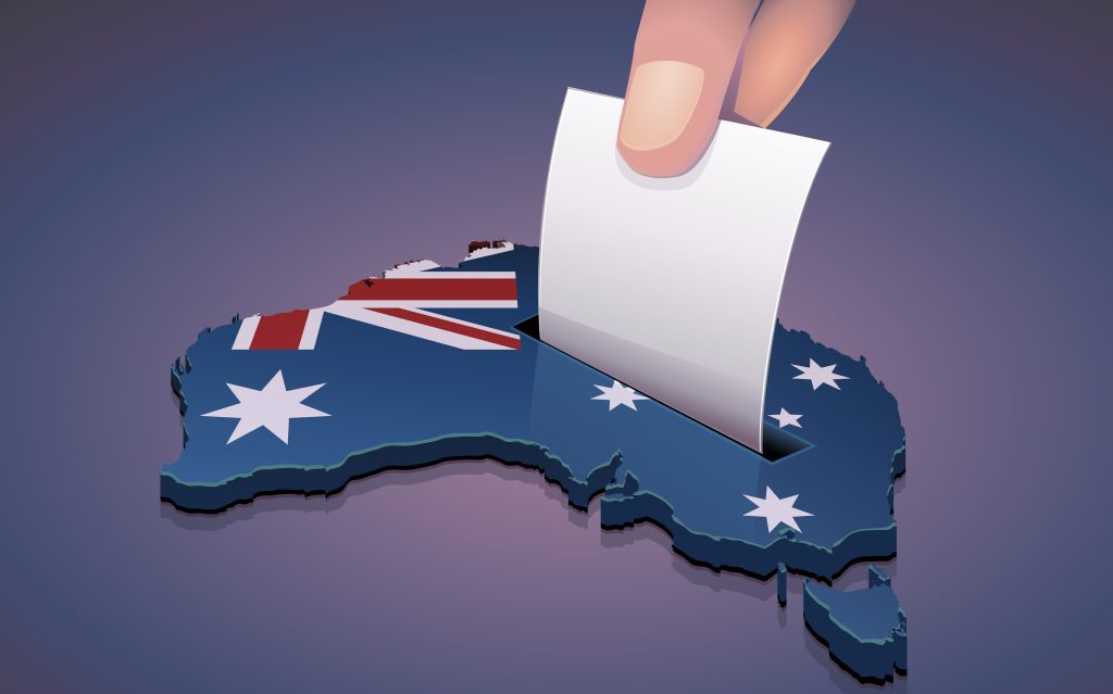 Fingers drop a voting form into a slot in a stylised image of Australia.