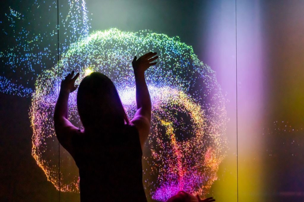 A woman waves her hands across an interactive wall of rainbow colours.