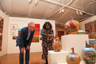 Man (Paul Fletcher) examining ceramic works of a woman (Judith Inkamala) in an art gallery