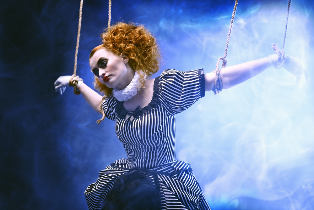 A woman on stage in a ruff lhas strings so she she is suspended like a puppet