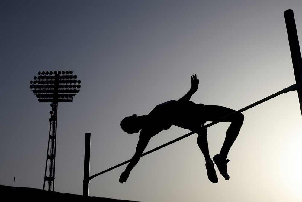 A pole vaulter is silhouetted against a darkening sky.