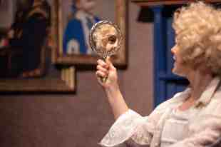 Erin Jean Norvill in a blonde wig as Dorian Gray gazes at himself/herself in a hand-held mirror.