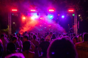A crowd dances at an outdoor club as red and purple lights shine down on them.