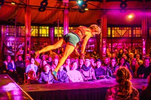 A female circus performer photographed mid-air with an audience looking on behind her.
