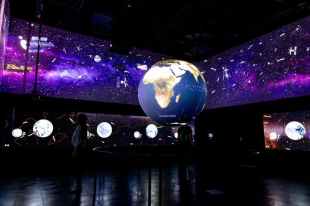 A dark exhibition space with a series of lit up globes hanging in it.