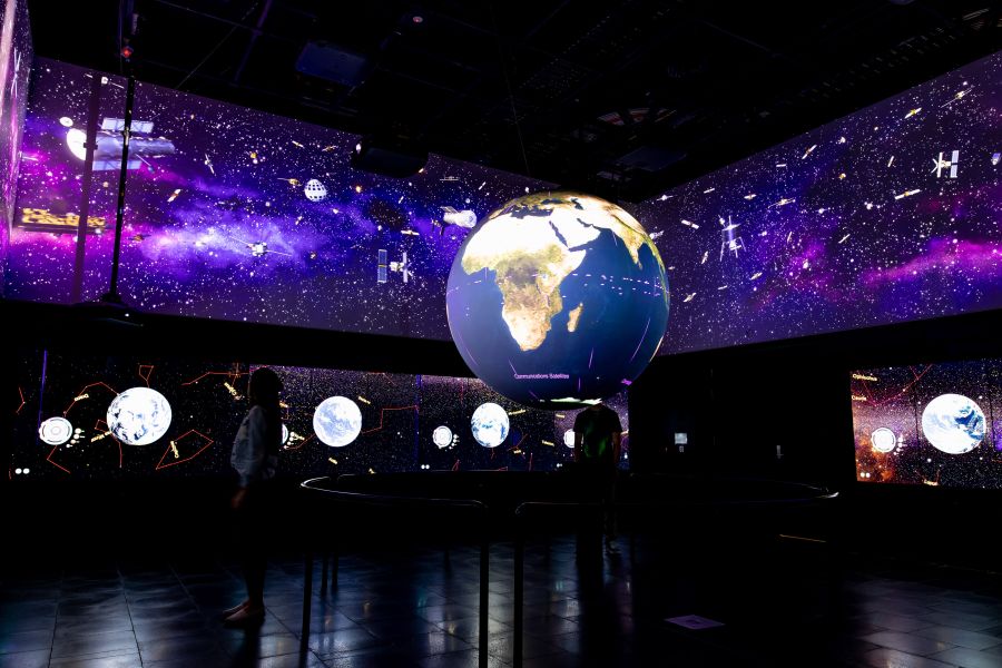 A dark exhibition space with a series of lit up globes hanging in it.