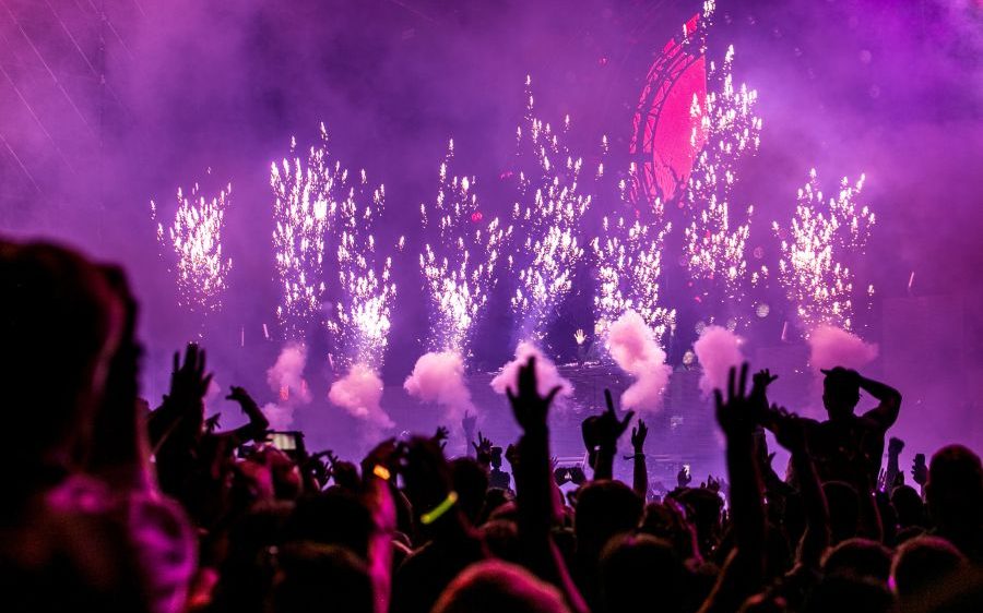 a large music concert crowd and stage with small fireworks being set off.