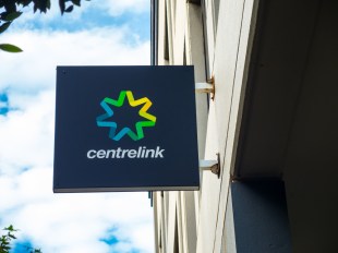 The Centrelink logo photographed against a cloud-dappled sky.