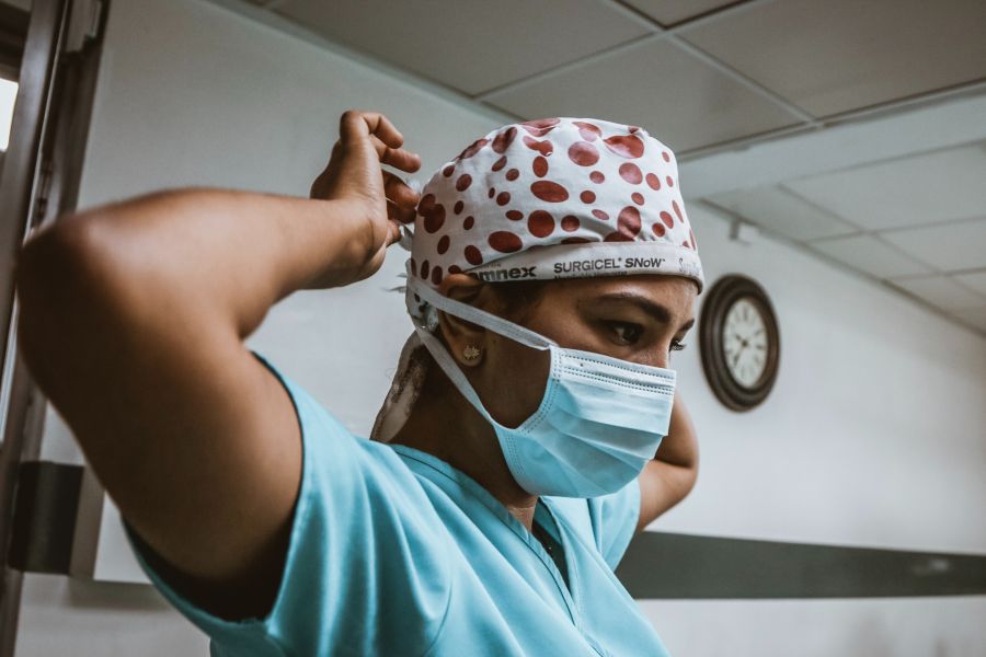 a health care worker adjusting a mask and surgical headscarf.