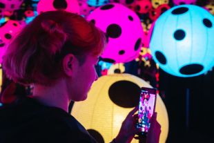A teenage girl in a darkened exhibition space taking a photo of artworks in it.