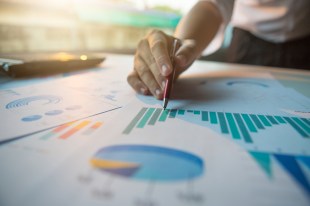 A hand holding a pen notates a spread of data shown in various graphs.