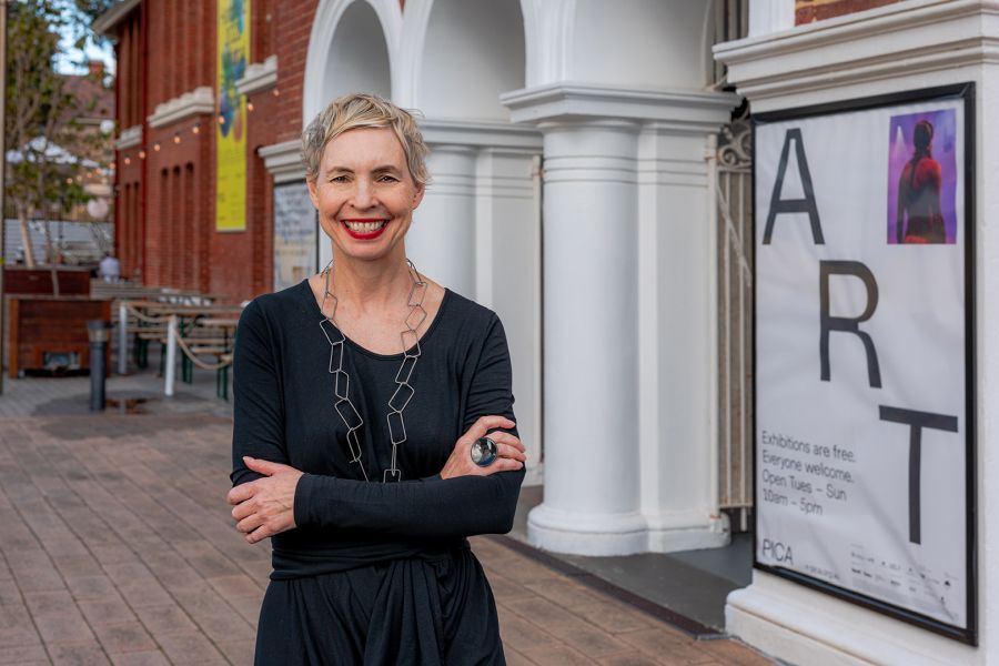 a woman with short blond hair wearing black, standing outside a building