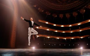 a male ballet dancer on stage, photographed mid-jump in mid-air