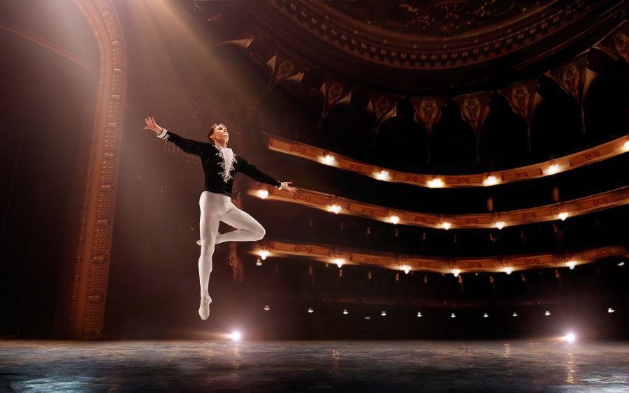 a male ballet dancer on stage, photographed mid-jump in mid-air
