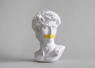 A marble bust sculpture of Michelangelo with a piece of yellow tape stuck over his mouth.