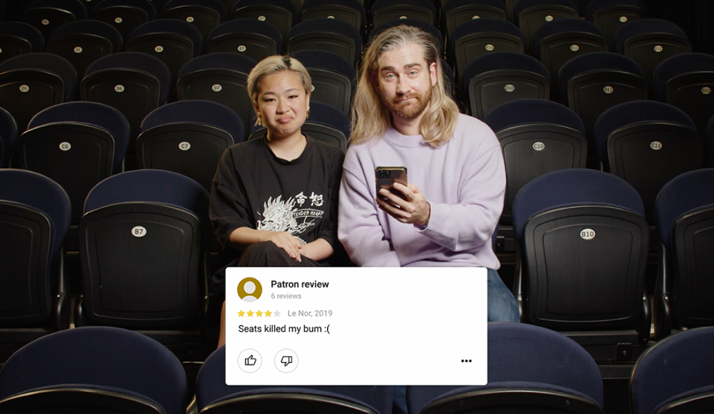 one female and one male person sitting together in an otherwise empty theatre looking at bad customer reviews on their phones.