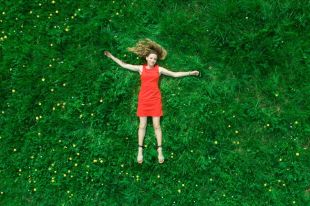 a girl in a red dress lying down in a bright green grassed field.