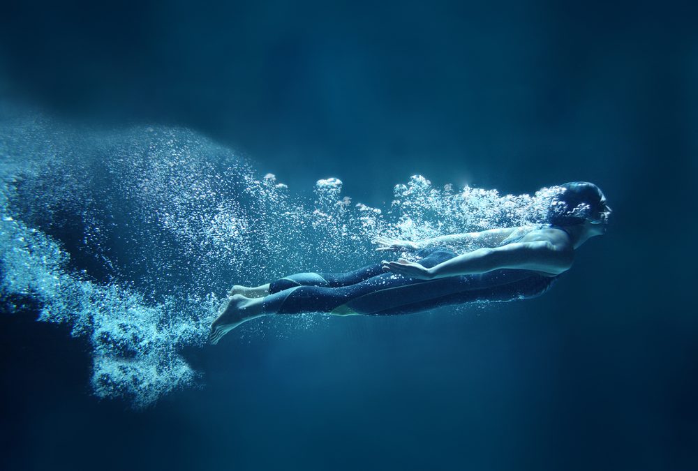 A dynamic underwater photo of a woman in a wetsuit surrounded by bubbles as she swims.