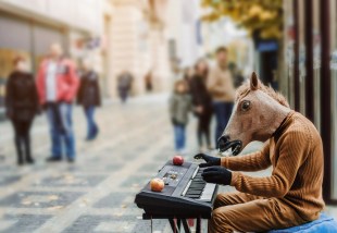 A horse-headed, mask-wearing busker plays a keyboard on the street.